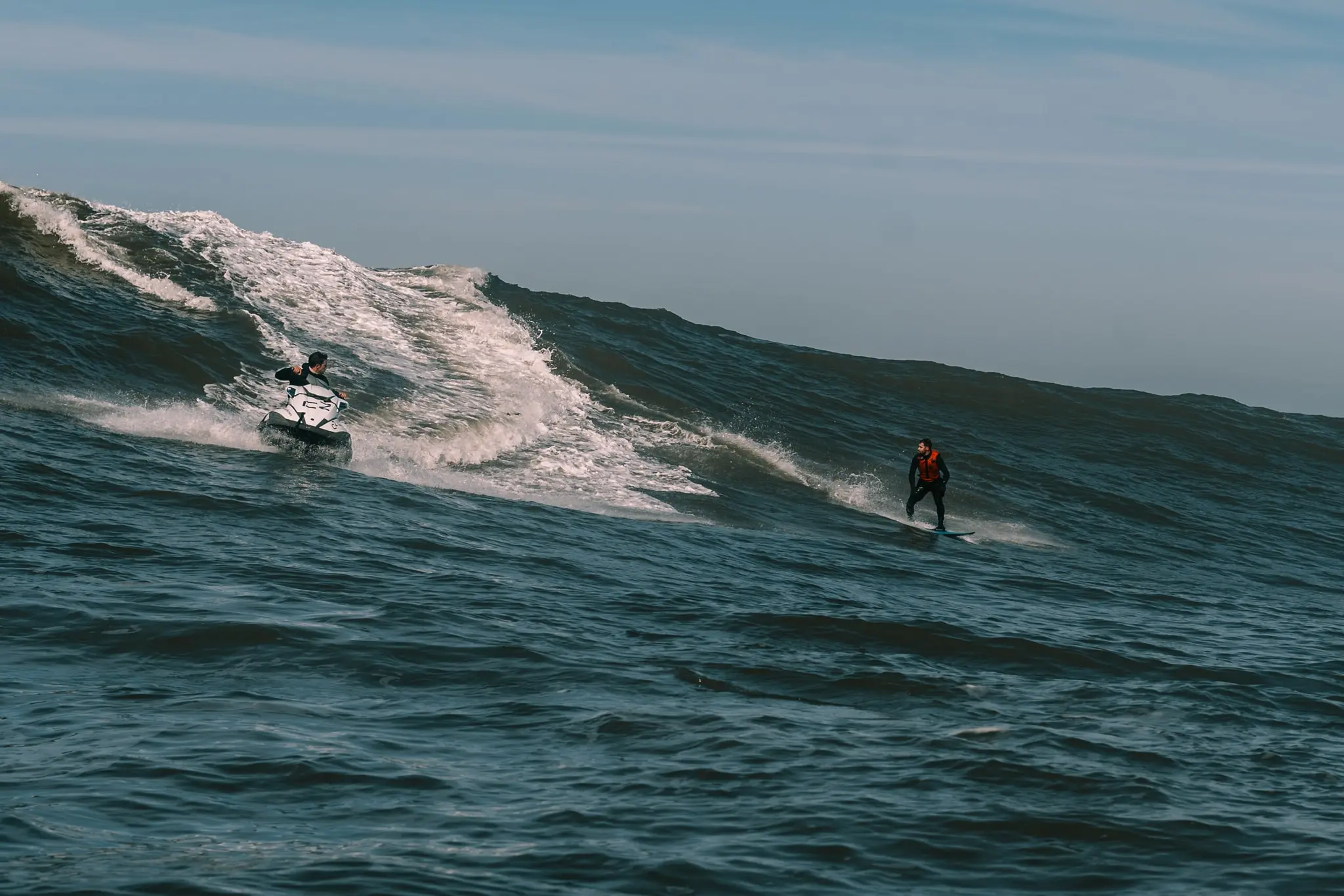 A surfer following a jet ski along a wave at Nazaré