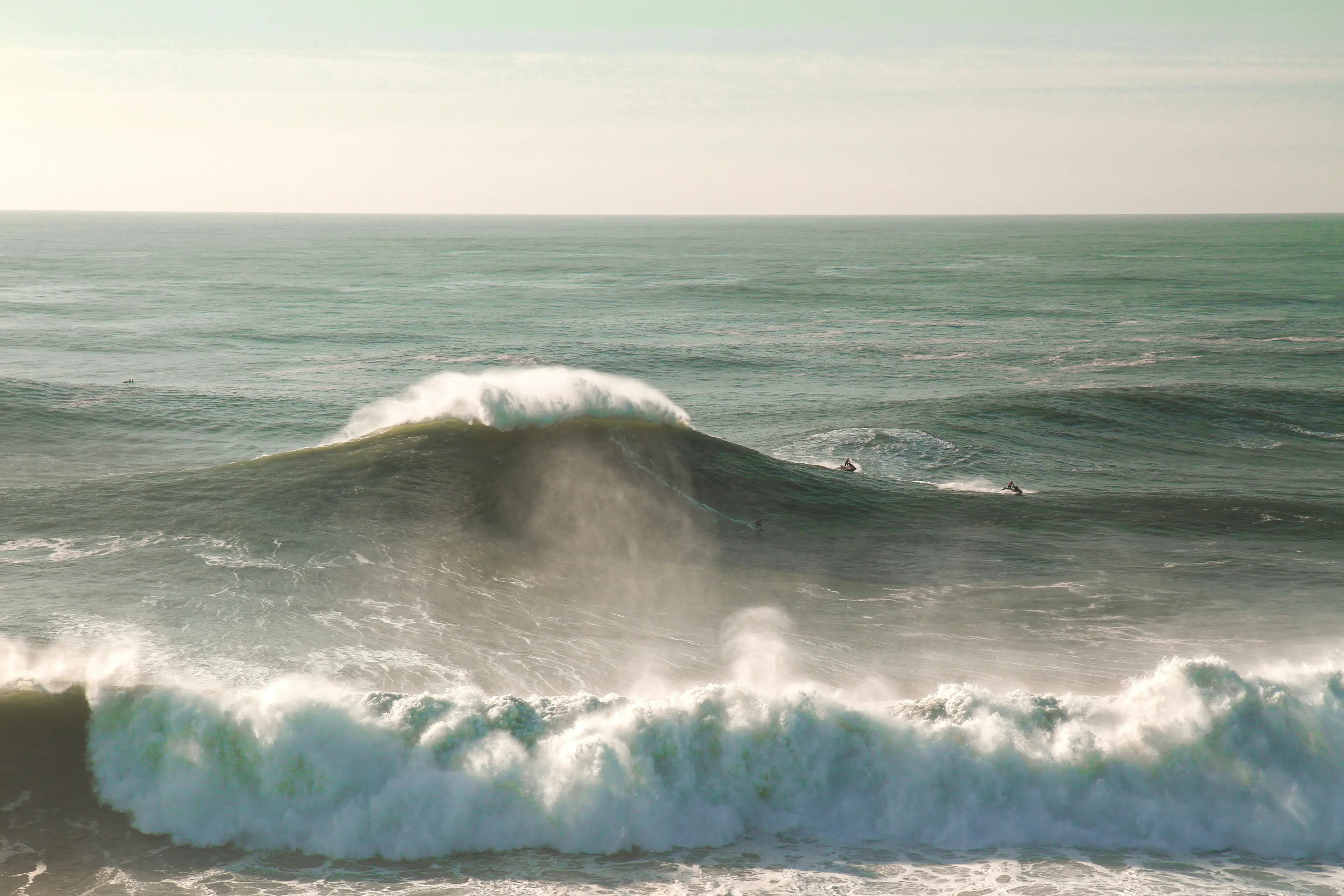 A powerful wave breaking offshore with surfers and jet skis nearby
